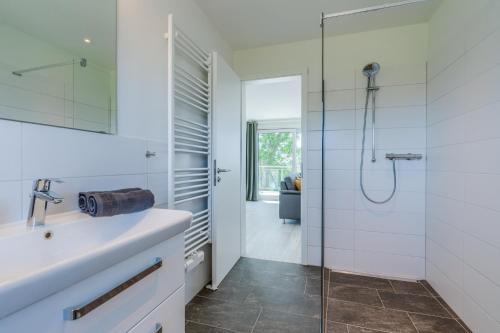 ein weißes Bad mit einer Dusche und einem Waschbecken in der Unterkunft Eiderstrand in Tielen