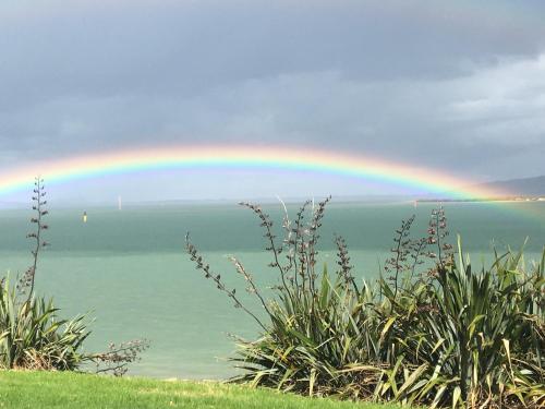 a rainbow in the sky over the ocean at Beach Lane Apartment in Whangarei