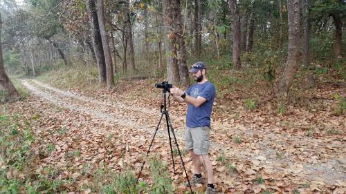 a man standing in the woods with a camera at Hotel Rhinoceros-Homestay in Sauraha