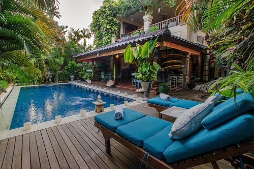 a house with a swimming pool with blue couches next to a house at Villa Kaja by Nagisa Bali in Seminyak