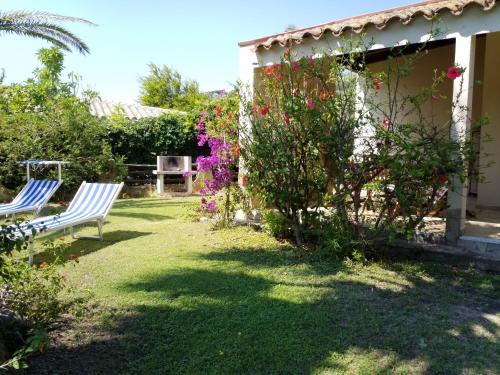 un patio con 2 sillas blancas y flores en Trilocale Turagri 45 en Costa Rei