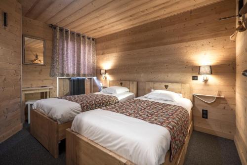 two beds in a room with wooden walls at Hôtel Restaurant U'Fredy in La Clusaz