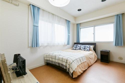een slaapkamer met een bed met blauwe gordijnen en een televisie bij Haneda Lex House in Tokyo