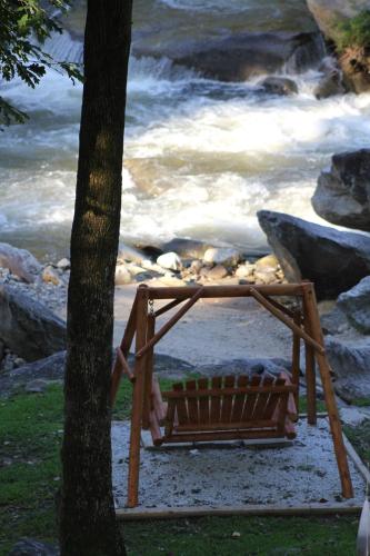 a wooden bench sitting next to a tree next to a river at The Evening Shade River Lodge and Cabins in Chimney Rock