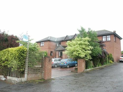 a house with cars parked in a parking lot at Herdshill Guest House in Wishaw