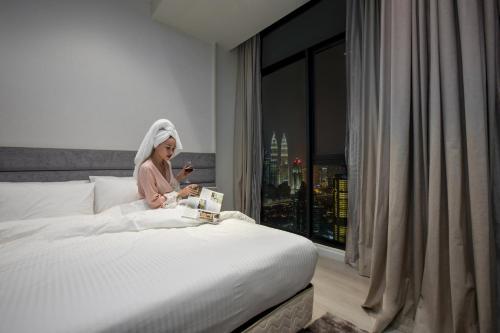 a woman sitting on a bed looking at her cell phone at Expressionz Suites By iHost Global in Kuala Lumpur