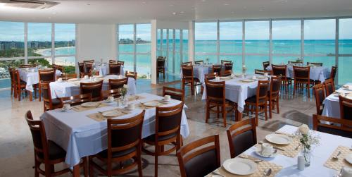 a restaurant with white tables and chairs and windows at Hotel Brisa Praia Pajuçara in Maceió