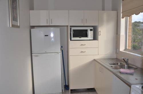 a white kitchen with a refrigerator and a microwave at Accommodation Sydney Kogarah 2 bedroom apartment with balcony in Sydney