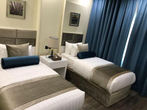 two beds in a hotel room with blue curtains at Golden Bujari AlUlaya Hotel in Al Khobar