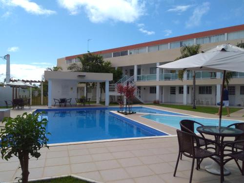 a swimming pool with a table and an umbrella next to a building at Flat 123 Bella Lunna in Guarajuba