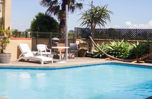 a swimming pool with chairs and a table and a table and chairs at The Beachcomber Hotel in Nelson