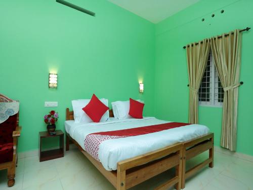 a bedroom with a bed with green walls and red pillows at Konark Homestay in Thekkady