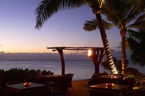 a restaurant with tables and palm trees and the ocean at Pacific Resort Aitutaki - Adults Only in Arutanga