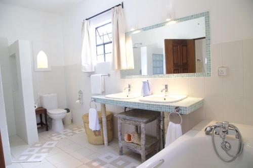 a bathroom with two sinks and a mirror and a toilet at Mwanana House in Watamu