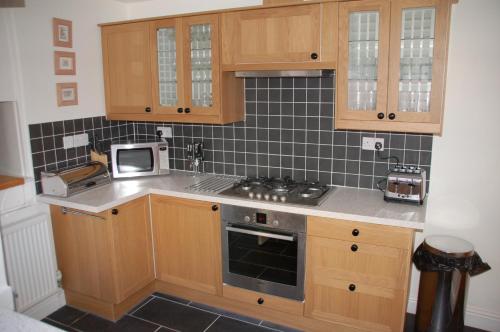 a kitchen with wooden cabinets and a stove top oven at Woodbine Cottage in Tenby