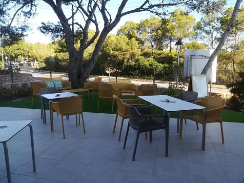 a patio with tables and chairs and a tree at Apartamentos Villa Primera in Cala Figuera