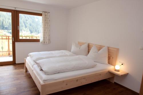 Schlafzimmer mit einem Bett mit weißer Bettwäsche und einem Fenster in der Unterkunft Schweinsteghof Urlaub auf dem Bauernhof in Sarntal