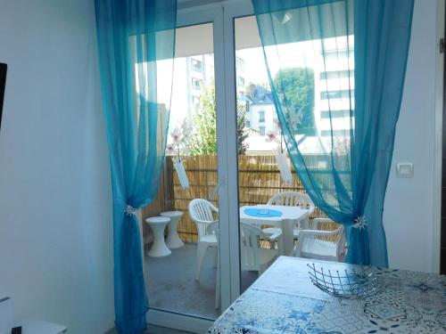 Habitación con balcón con cortinas azules, mesa y sillas. en Le petit nid, en Lourdes