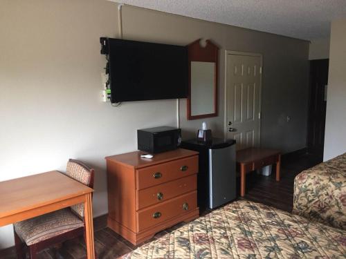 ein Hotelzimmer mit einem Bett, einer Kommode und einem TV in der Unterkunft Briarwood Inn in Pine Bluff