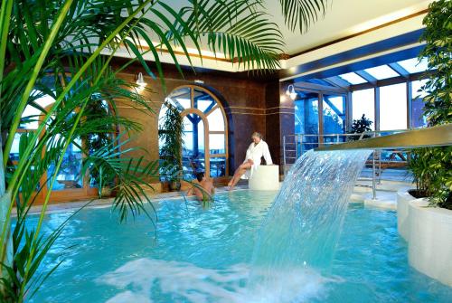 a man sitting in a chair next to a pool with a fountain at Vital&Spa Resort Szarotka in Duszniki Zdrój