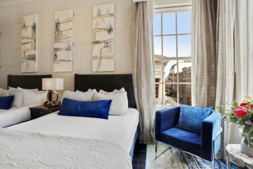 a bedroom with two beds and a blue chair at La Galerie French Quarter Hotel in New Orleans