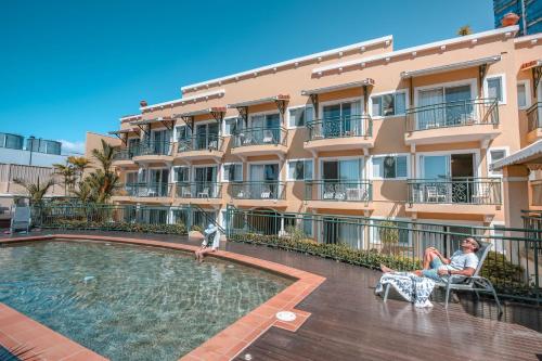 a couple sitting in chairs by a swimming pool in front of a building at Il Palazzo Holiday Apartments in Cairns