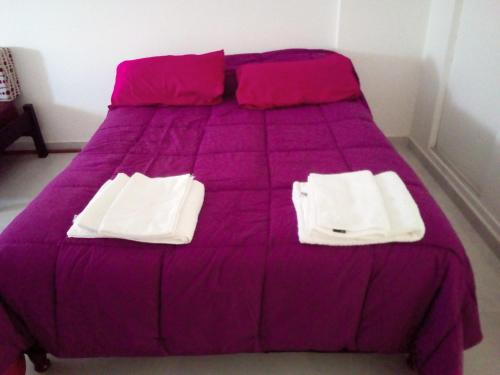 Una cama con sábanas moradas y toallas blancas. en Monoambiente Madryn en Puerto Madryn