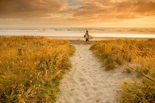 un hombre caminando por un camino a la playa con una tabla de surf en Tasman Holiday Parks - Beachaven, en Waihi Beach