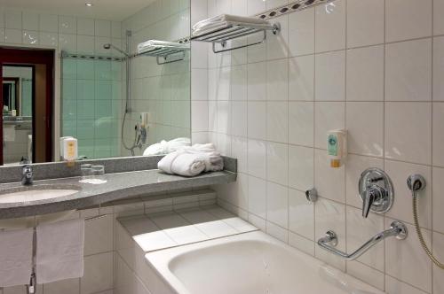 a bathroom with a tub, sink and mirror at Mercure Hotel Trier Porta Nigra in Trier