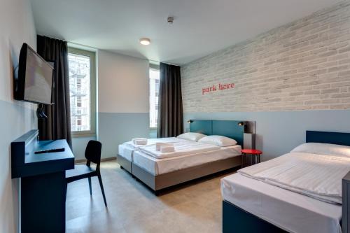 a bedroom with two beds and a desk and a tv at MEININGER Milano Lambrate in Milan