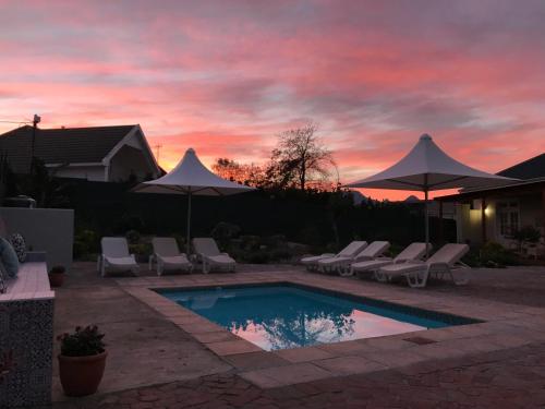 a pool with chairs and umbrellas with a sunset at Waterstone Lodge in Somerset West