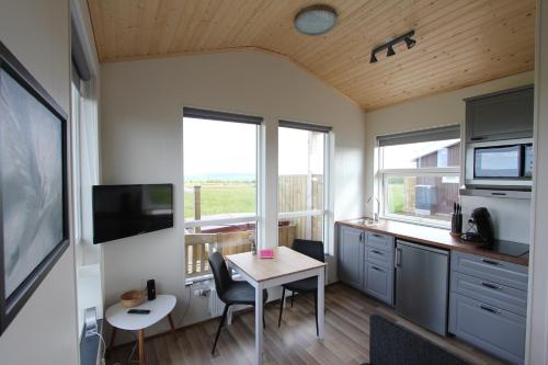 una pequeña cocina con mesa y algunas ventanas en Blue View Cabin 5B With private hot tub, en Reykholt
