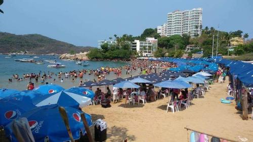 a crowd of people on a beach with blue umbrellas at Costa Miramar in Acapulco