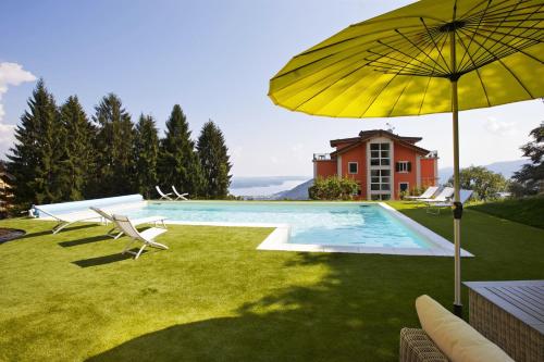 una casa y una piscina con sombrilla y sillas amarillas en Residence alle Ville, en Miazzina