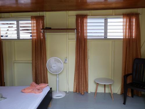 a room with two windows with curtains and a fan at Sea n sun Guest House in Caye Caulker