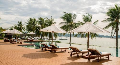 a pool with chairs and umbrellas next to the water at Que Toi Village Resort Phu Yen in Song Cau