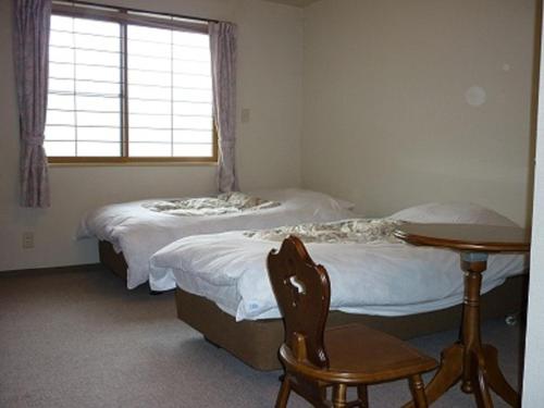 two beds in a room with a table and a window at Stayful House Nakamachi in Hakuba