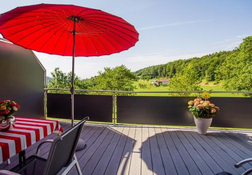 een patio met een rode parasol en een tafel en stoelen bij Ferienwohnung Streifinger in Freyung