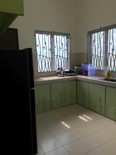 a kitchen with green cabinets and windows in a room at PATIN GUEST HOUSE @DESA TELOK IRA, TEMERLOH PAHANG in Kampong Paya Kerinau