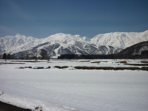 a snow covered field with mountains in the background at Stayful House Nakamachi in Hakuba