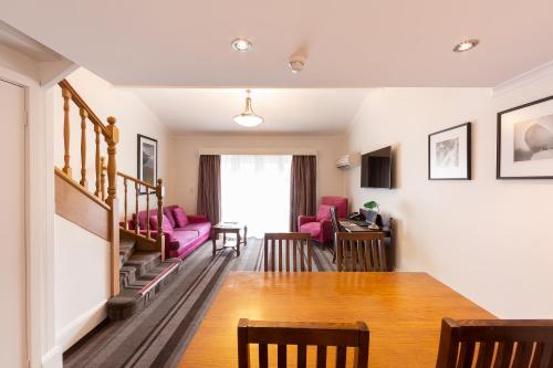 a living room with a dining room table and pink chairs at Mercure Canberra in Canberra