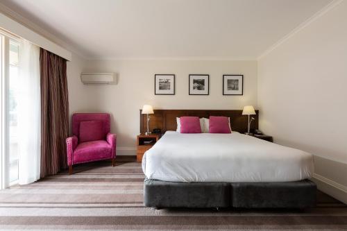 a bedroom with a bed and a pink chair at Mercure Canberra in Canberra