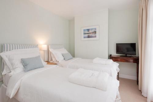 a white bedroom with two beds and a television at Sea Breeze Cottage with Parking in Brighton & Hove