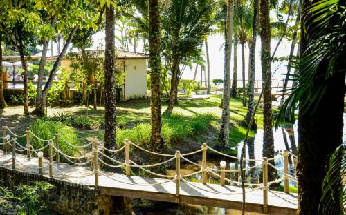 a wooden bridge in a garden with palm trees at Aldeia do Mar Sensorial Hotel in Itacaré