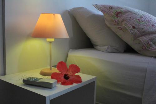 uma lâmpada e uma flor vermelha numa mesa ao lado de uma cama em Pousada Arraial Caribe em Arraial do Cabo