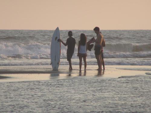 three people standing on the beach with a surfboard at Swell in El Paredón Buena Vista