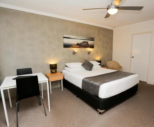 a hotel room with a bed and a desk and a table at Bella Villa Motor Inn in Forster