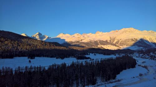 a snow covered mountain range with a river and trees at Schloss Hotel & Spa Pontresina in Pontresina