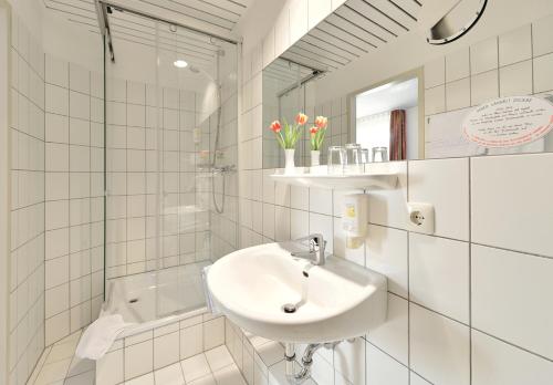 Hotel Haus Kronenthal في راتينغن: حمام أبيض مع حوض ومرآة