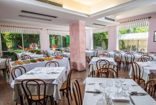 un restaurante con mesas y sillas blancas y ventanas en Hotel Le Querce, en Senigallia